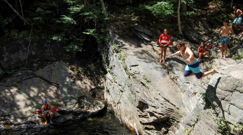 Campers jumping off a rock into water on an off-camp trip