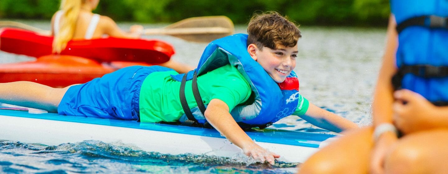 Boy laying on stand up paddleboard at Camp Waziyatah