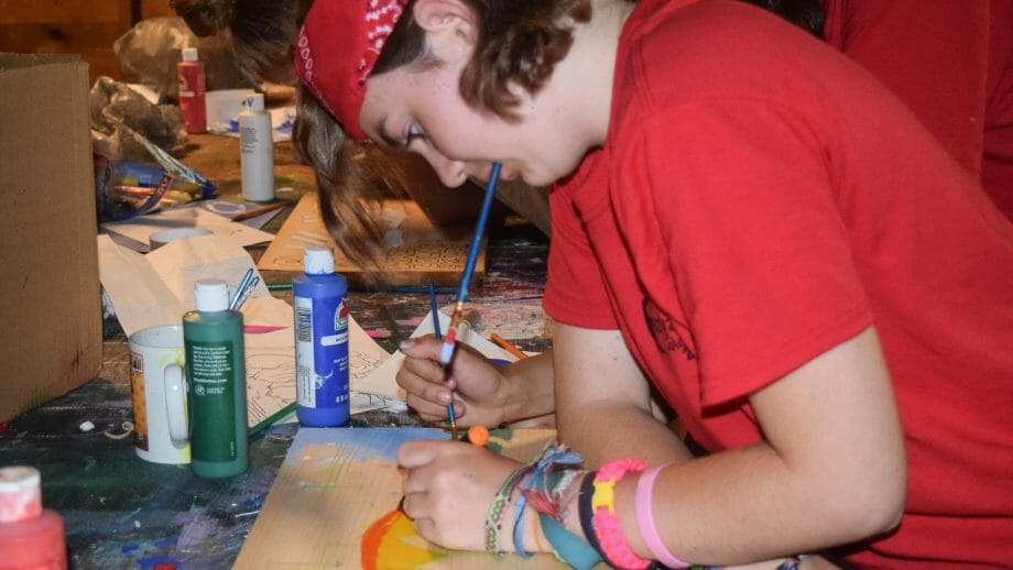 Camper painting a piece of wood at arts and crafts