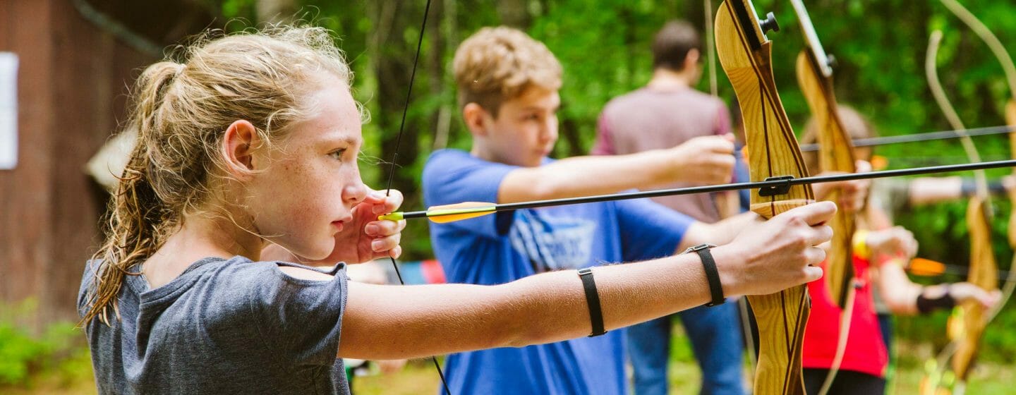 Girl with other campers practicing archery shots