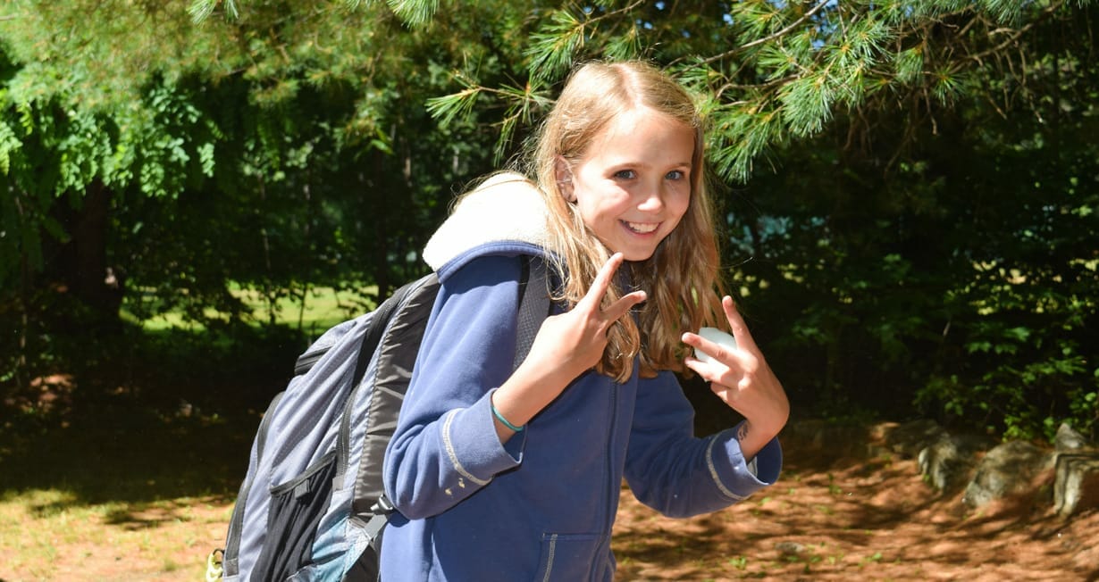 Camper giving the peace sign and wearing a backpack on arrival day
