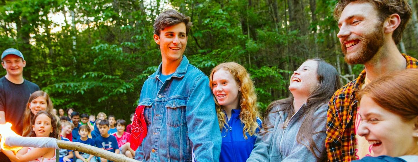 Staff and campers lighting a torch in the campfire