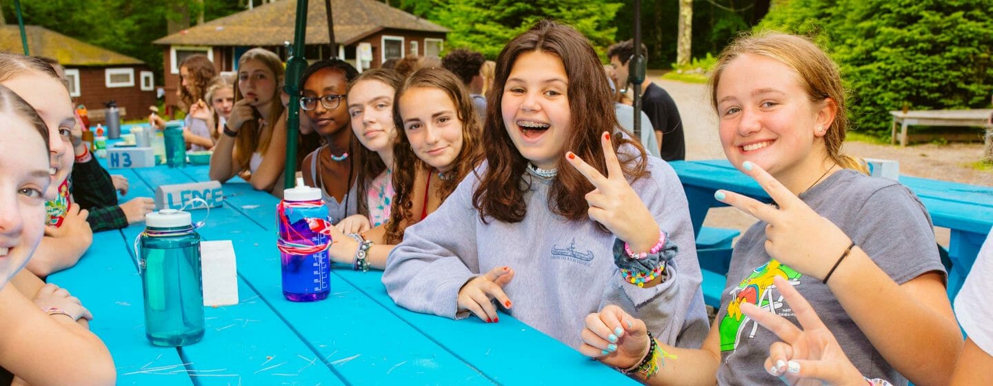 Girls sitting at the dining hall picnic tables giving a peace sign