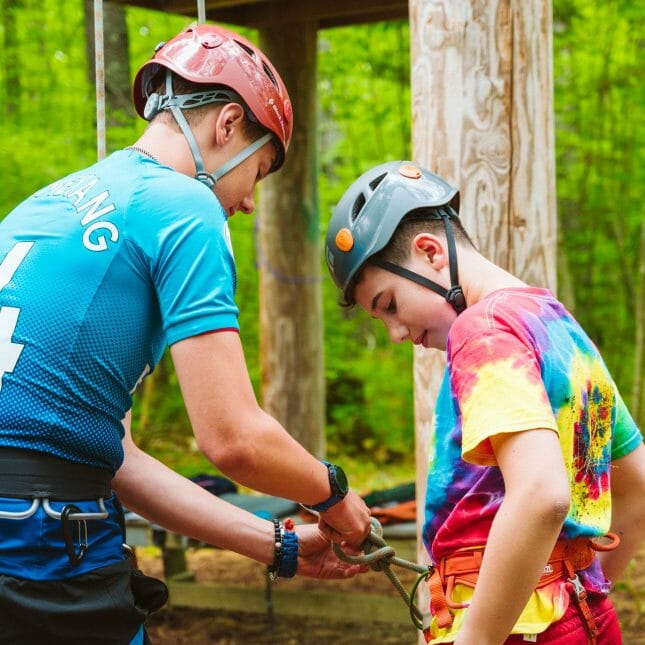 Climbing staff securing a camper's harness by the ropes course