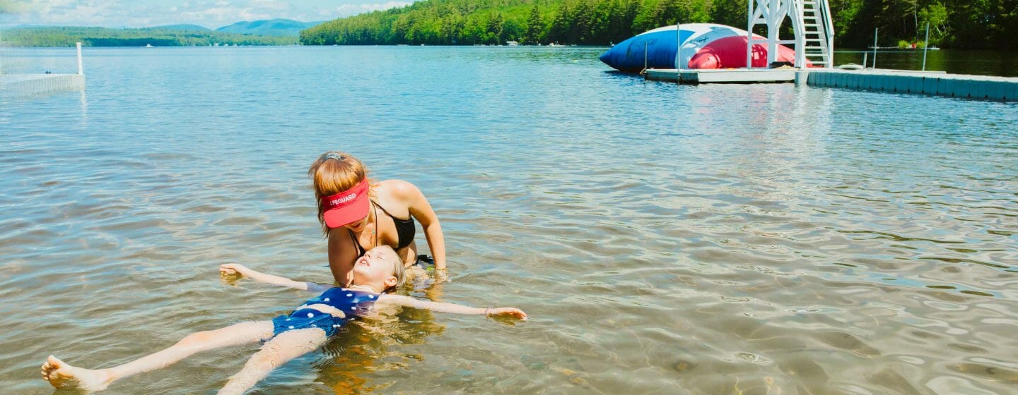 Lifeguard giving swim lessons to a girl in the lake